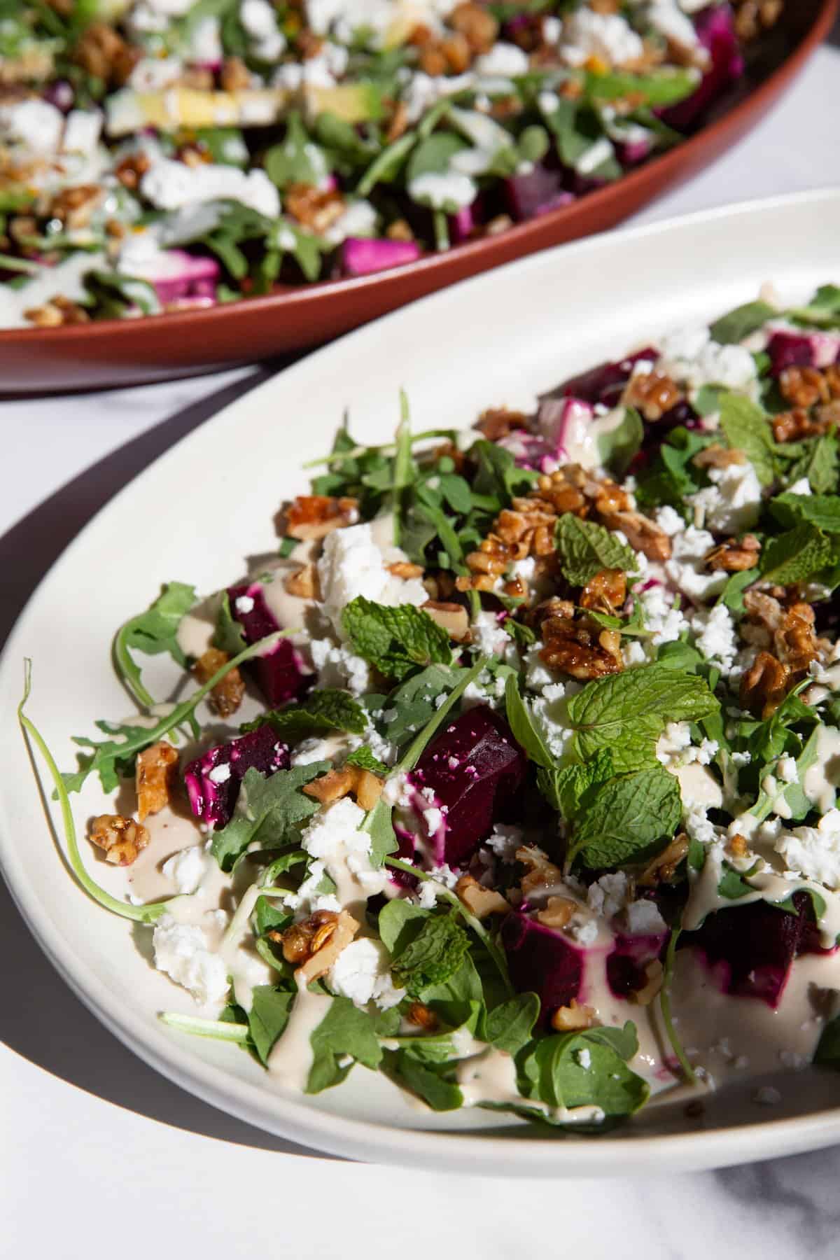 two roasted beet salads in serving trays finished with various toppings.