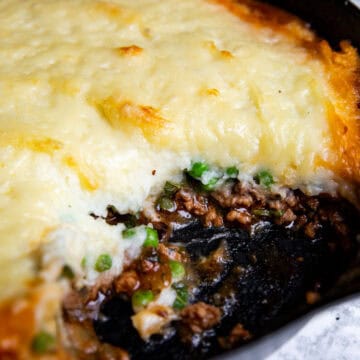 skillet shepherd's pie with lamb in a cast iron pan with a serving taken out to show the rich center
