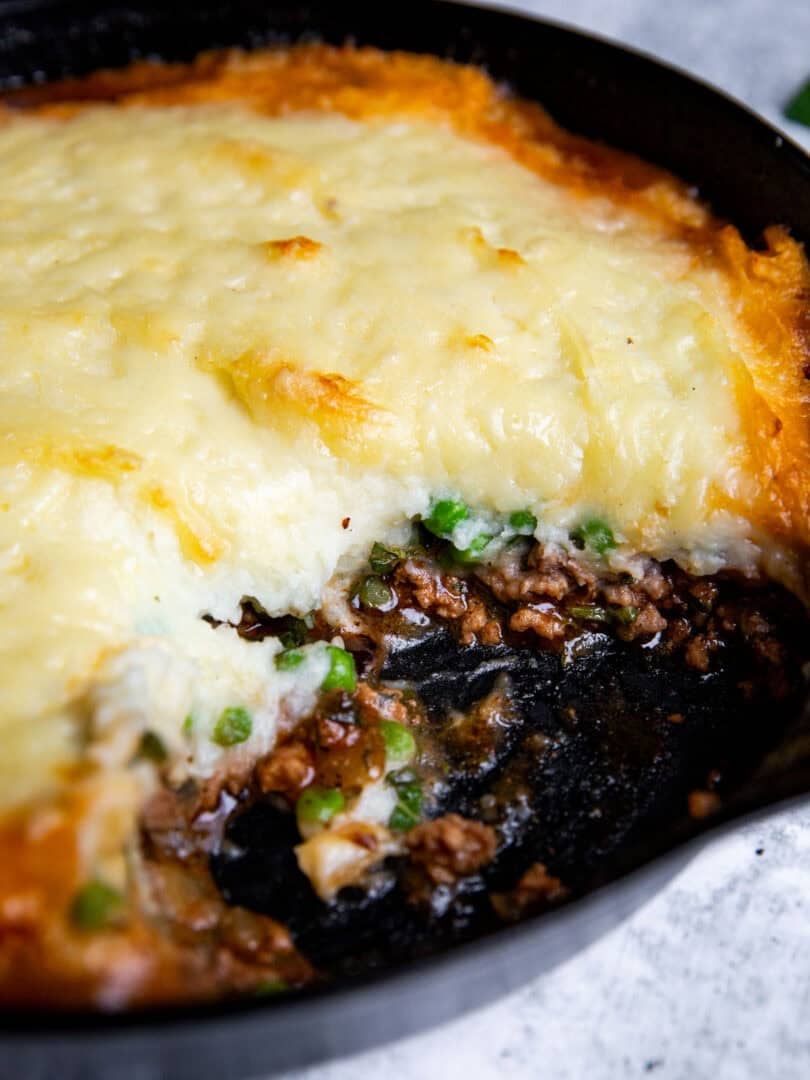 skillet shepherd's pie with lamb in a cast iron pan with a serving taken out to show the rich center