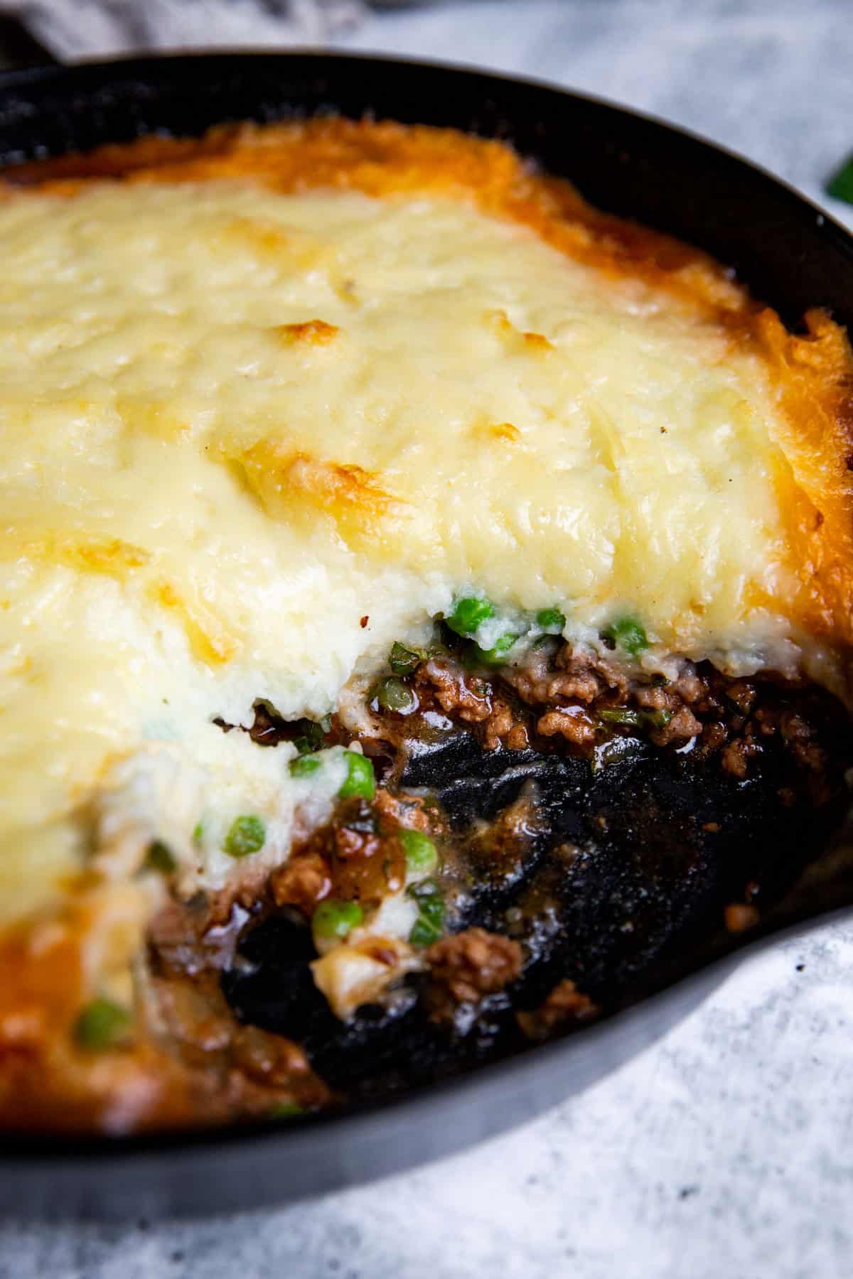skillet shepherd's pie with lamb in a cast iron pan with a serving taken out to show the rich center