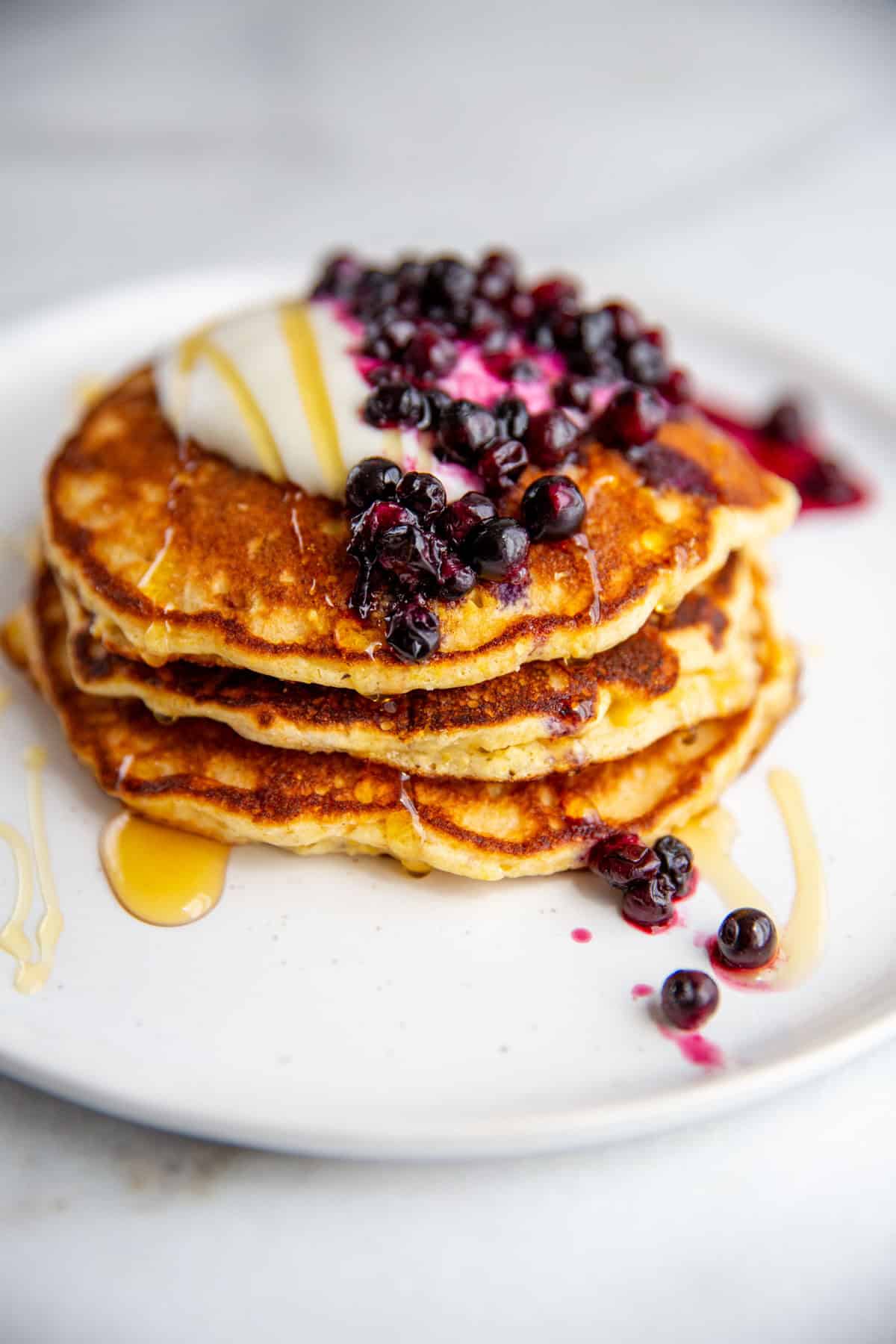 A stack of gluten-free cornmeal pancakes topped with butter and blueberries.