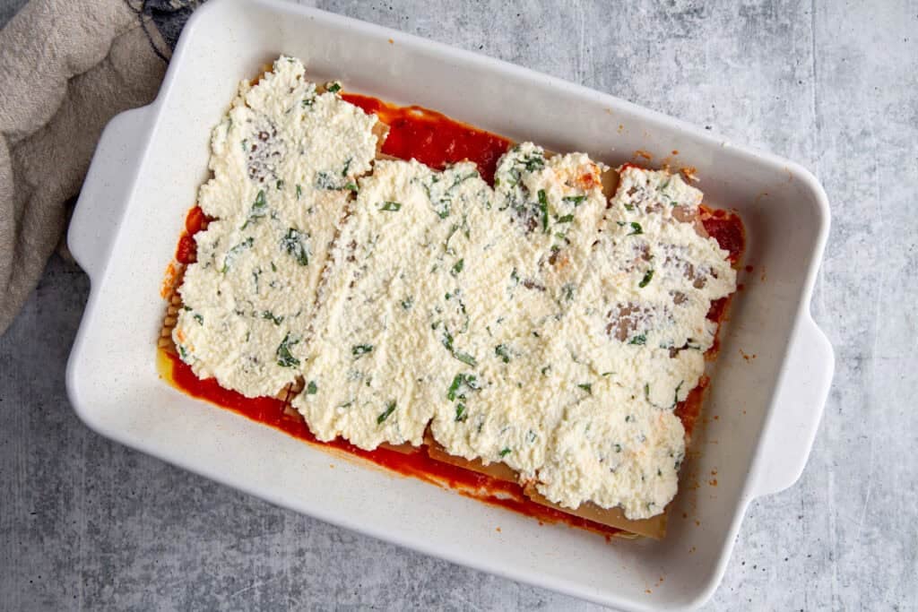 Ricotta mixture atop the first layer of sauce and noodles in a casserole dish.