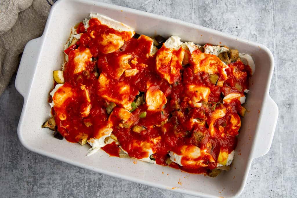 Marinara sauce poured on top of the layers of roasted veggie lasagna in the casserole dish.