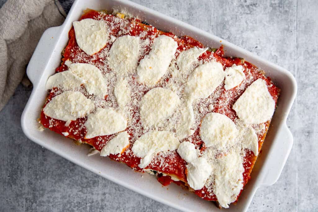 The final layer of mozzarella and parmesan cheeses atop the sauce and noodles in roasted veggie lasagna that is gluten-free.
