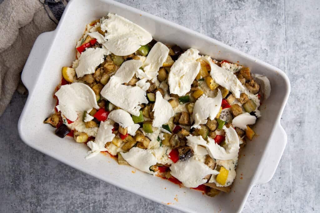 Roasted veggies and mozzarella cheese resting atop the layer of sauce, noodles, and ricotta in veggie lasagna.
