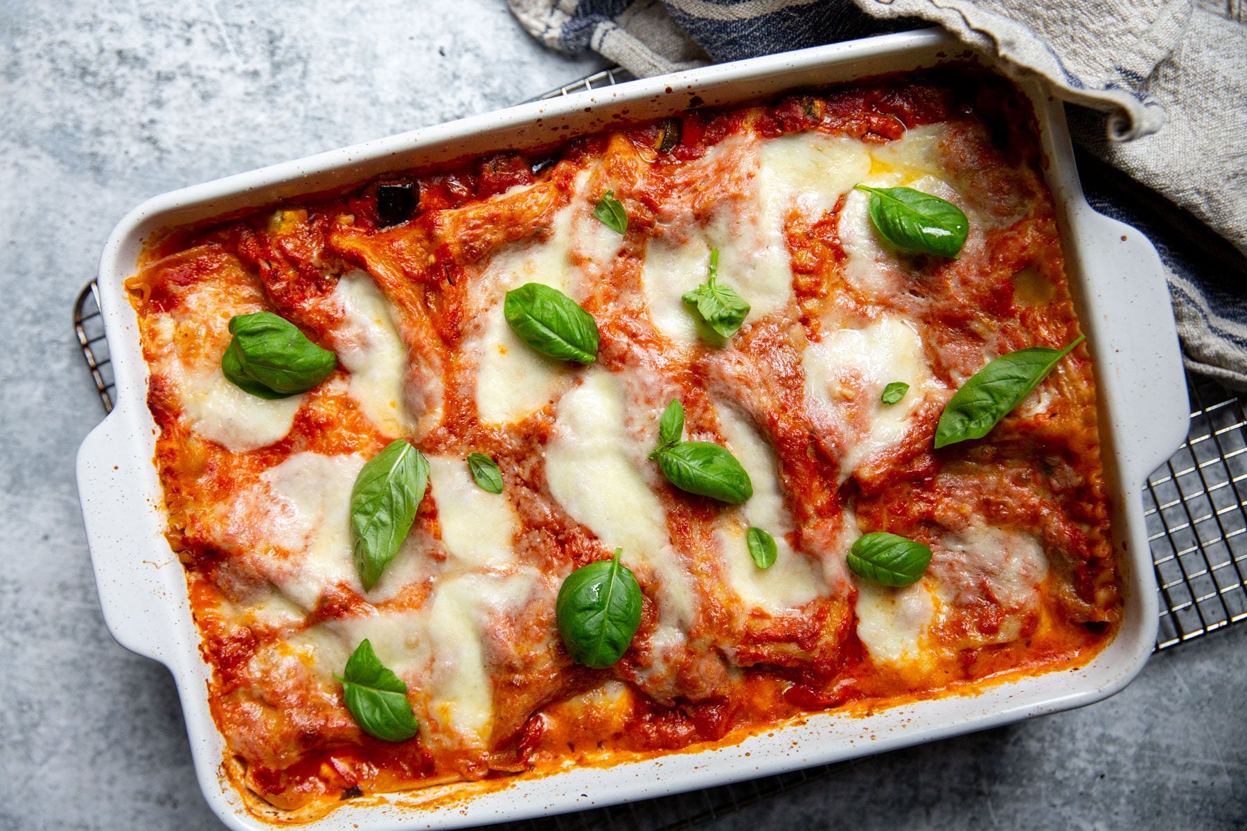 A white casserole dish filled with gluten-free vegetarian lasagna and topped with sauce, cheese and basil.