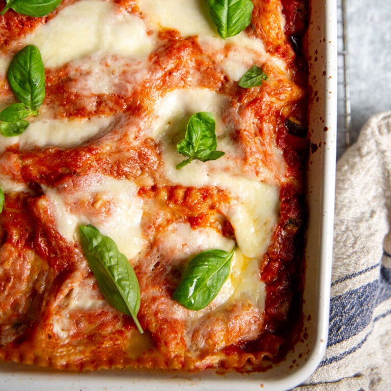 Gluten-free vegetable lasagna topped with basil sprigs in a white casserole dish.