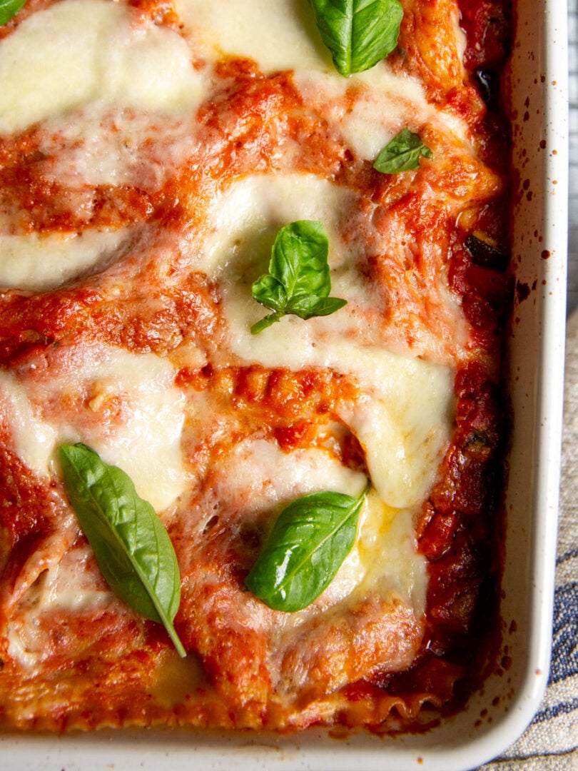 Gluten-free vegetable lasagna topped with basil sprigs in a white casserole dish.
