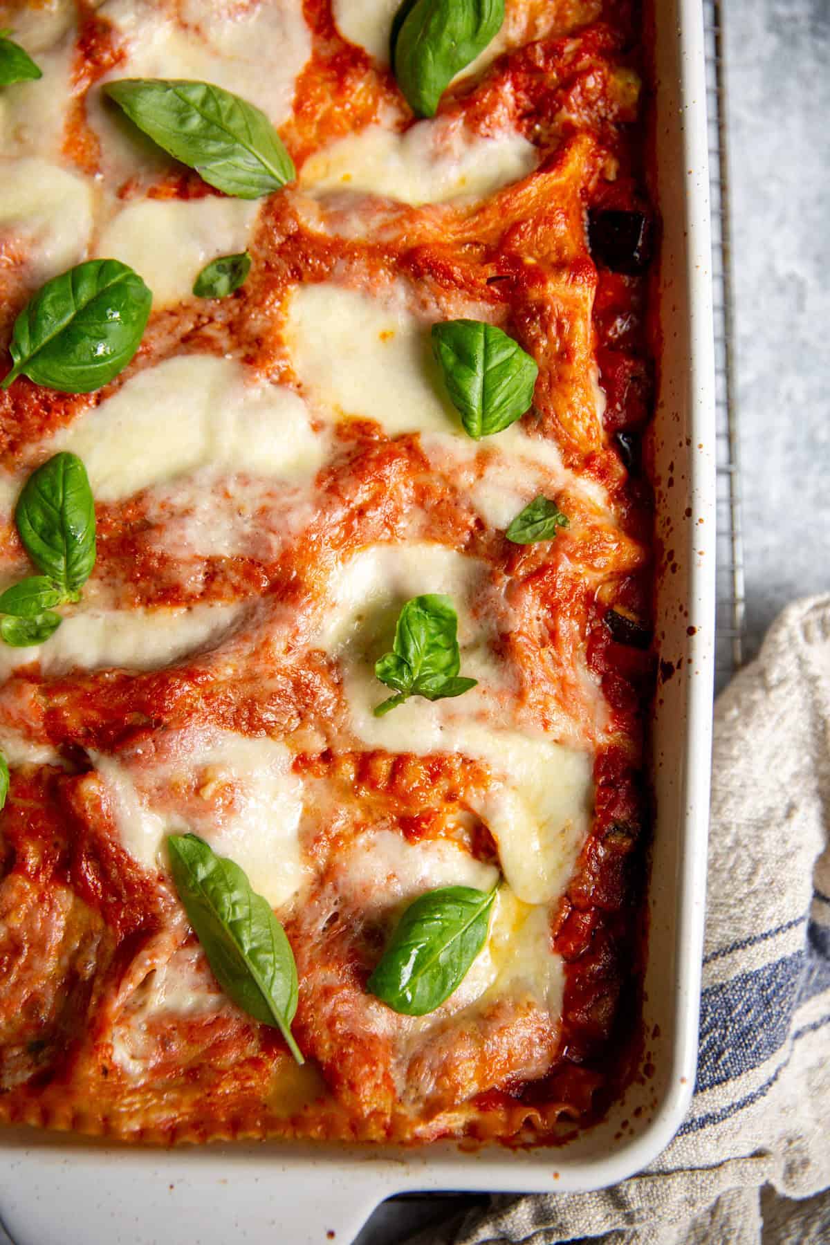 A close up image of roasted veggie lasagna showing the melted cheese and sauce and basil.