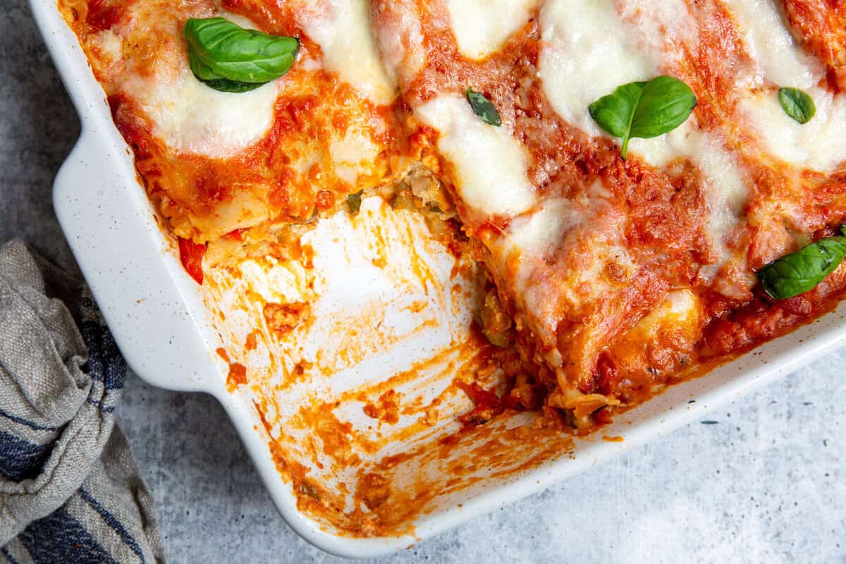 A slice of veggie lasagna removed from a white casserole dish.