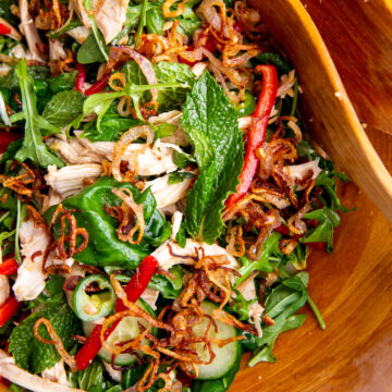 chicken, herbs, and greens in a wooden bowl topped with crispy shallots for a Vietnamese inspired salad