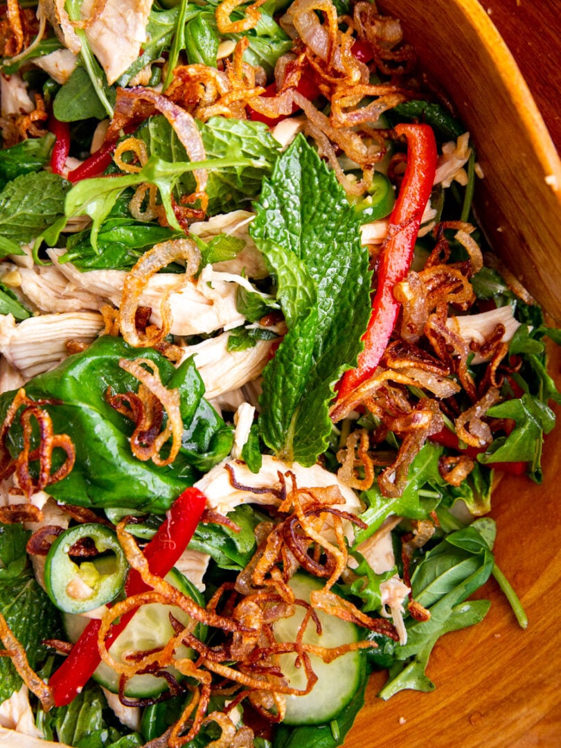 chicken, herbs, and greens in a wooden bowl topped with crispy shallots for a Vietnamese inspired salad