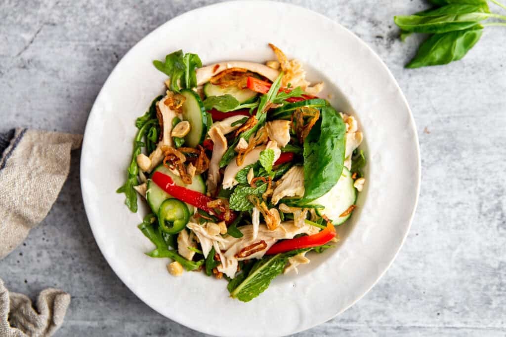 Vietnamese inspired chicken salad with herbs, peppers, and a chili lime dressing in a white bowl topped with crispy shallots and peanuts.