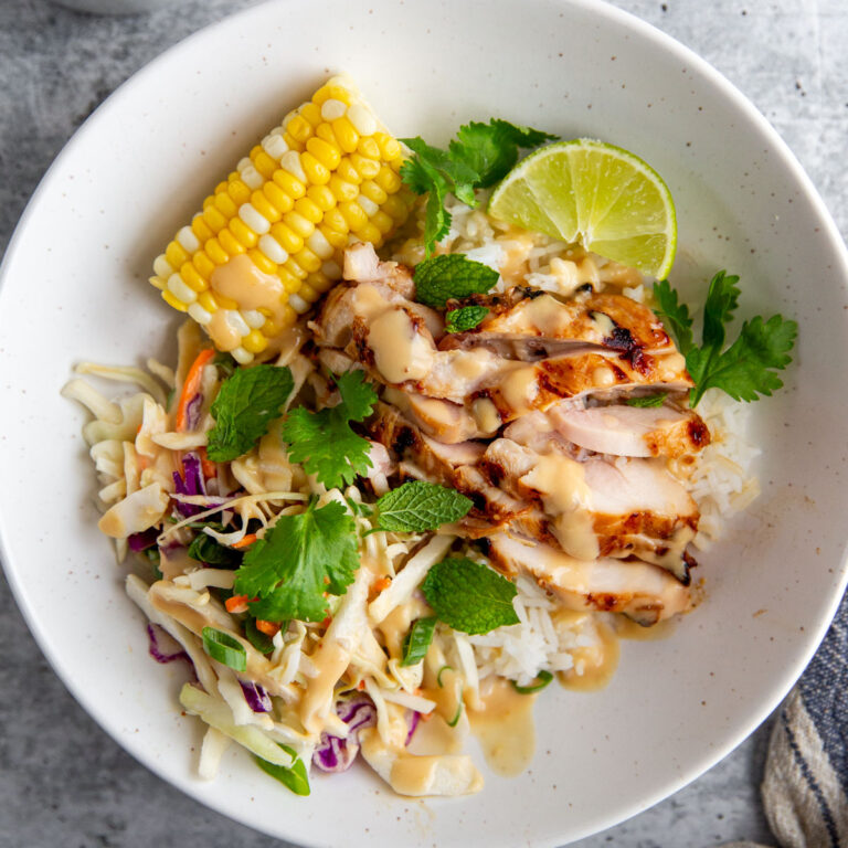 grilled miso chicken in a bowl with corn, greens, and a lime wheel.