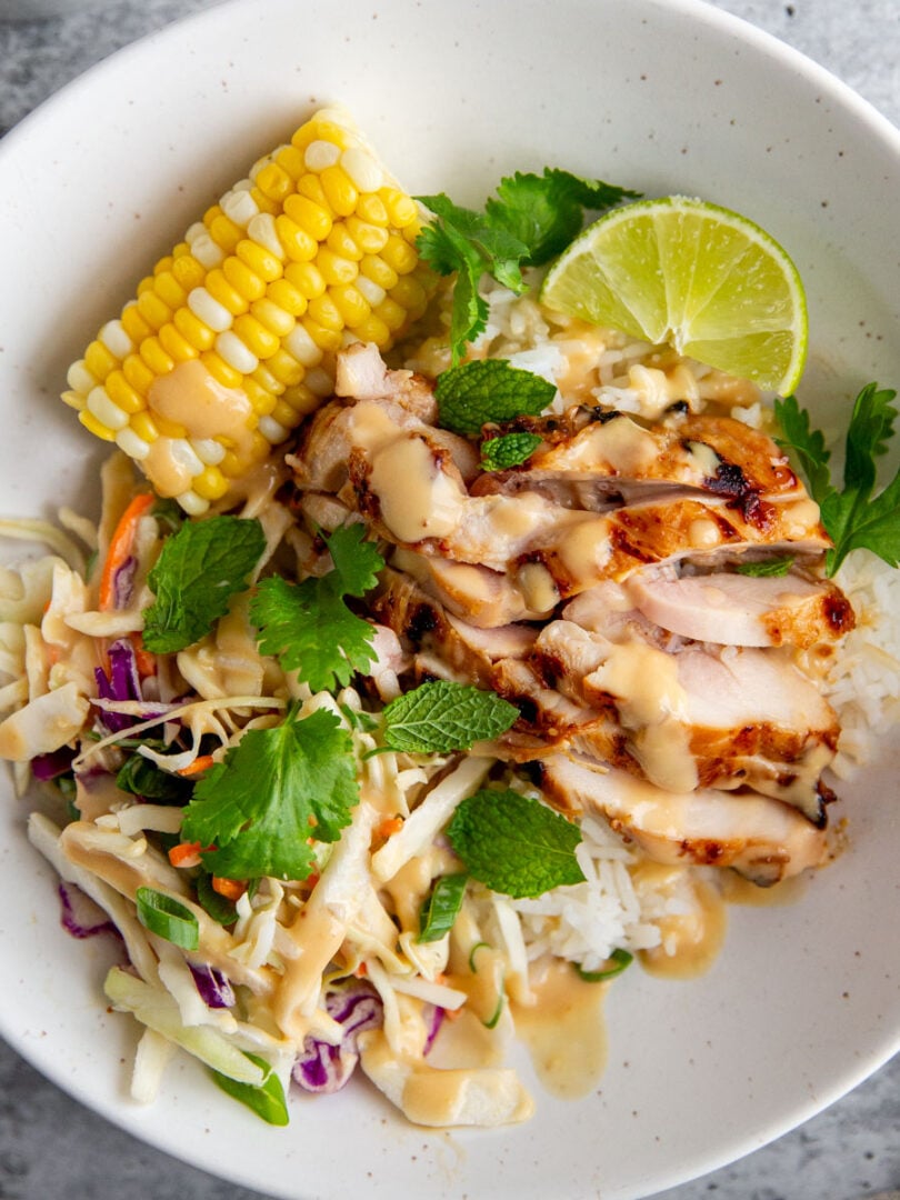 grilled miso chicken in a bowl with corn, greens, and a lime wheel.