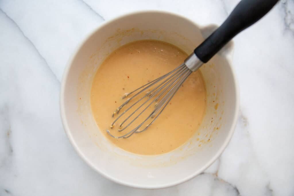 A mixing bowl filled with miso dressing combined with a whisk. 