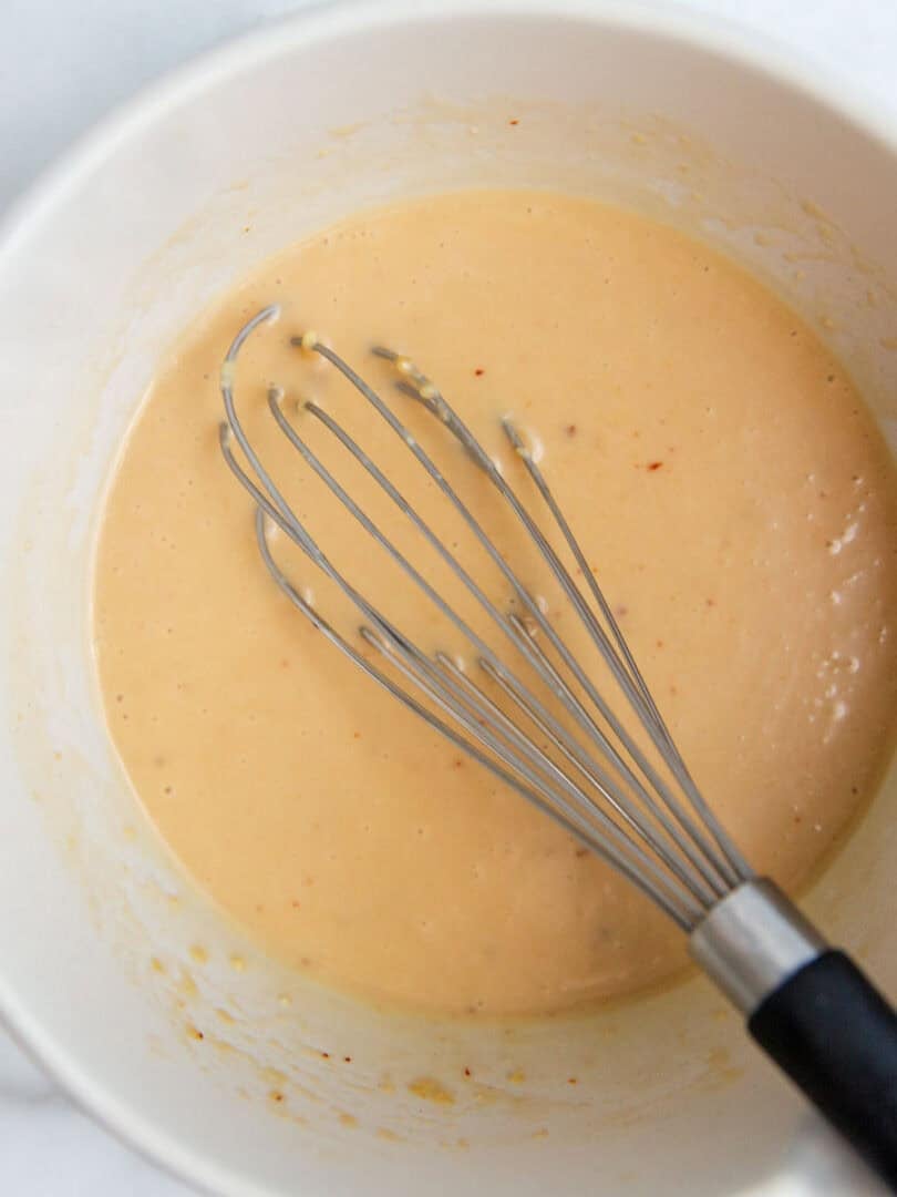A bowl of miso dressing with a whisk resting on the side.