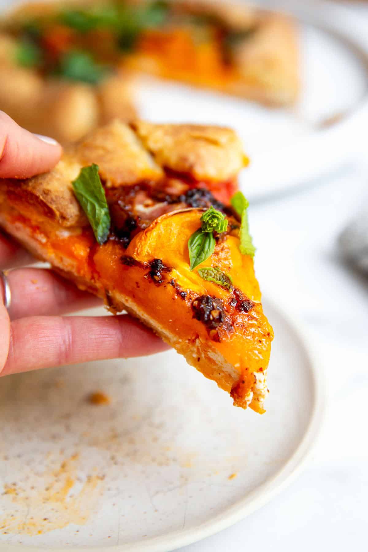 a hand holding a slice of tomato galette above a plate. 