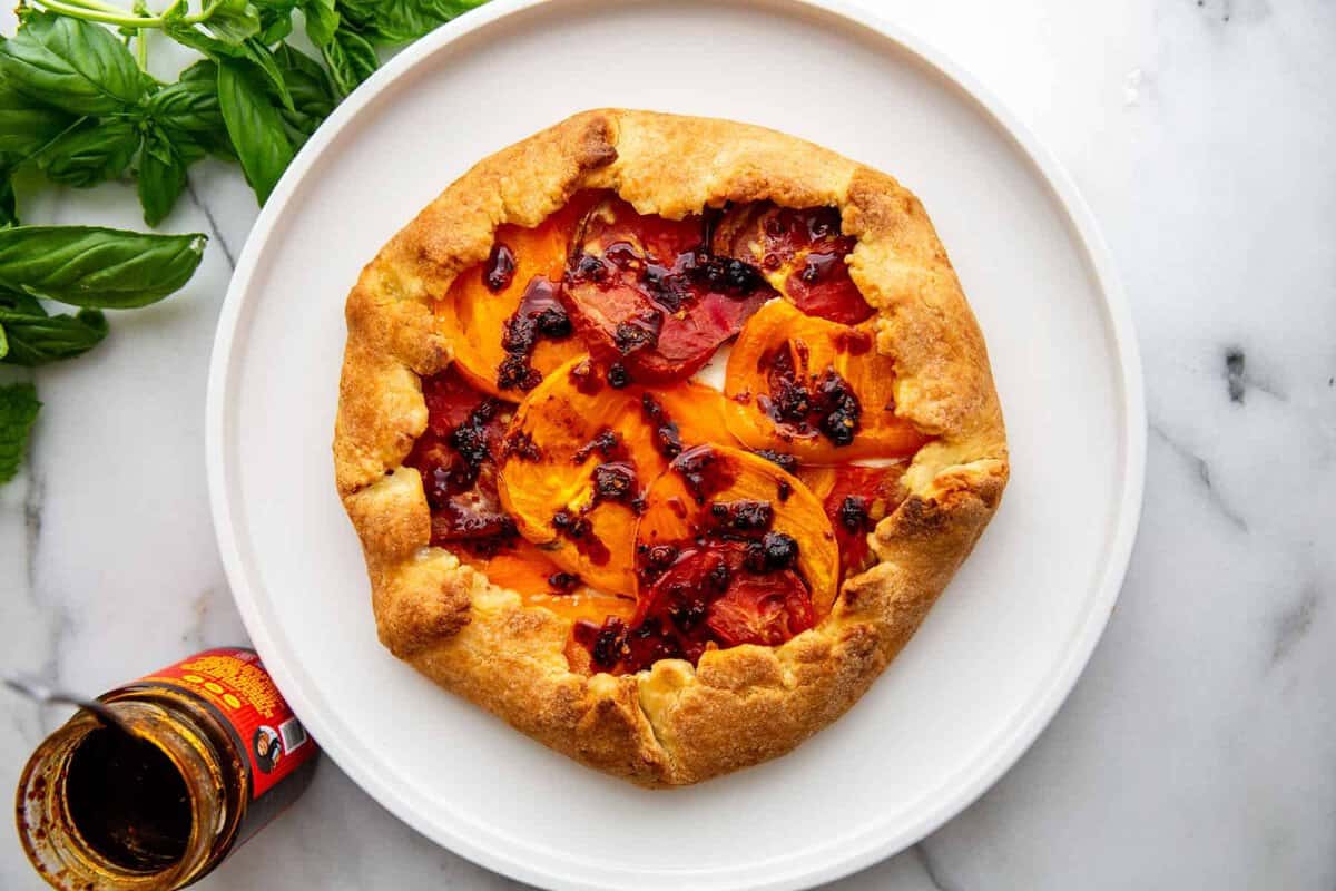 the baked tomato galette on a white plate ready to finish with the mint and chili crisp. 
