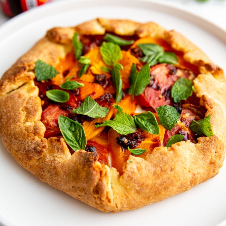 A tomato galette on a white plate topped with fresh mint and chili crisp.