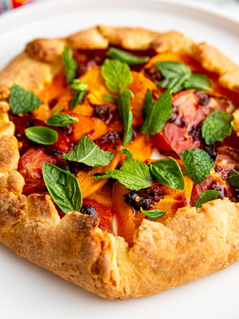 A tomato galette on a white plate topped with fresh mint and chili crisp.